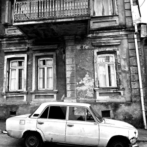 Monochrome, vintage car standing in front of a Nostaligian building with a distinctive balcony