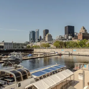 Panorama de la skyline de la ville de Montréal au-dessus d'un fleuve en journée avec des bâtiments urbains.