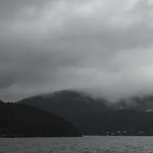 Moody seascape with a mountainous backdrop under a dense gray cloud cover as seen from a passenger ferry crossing Moody seascape with a mountainous backdrop under a dense gray cloud cover as seen from a passenger ferry crossing