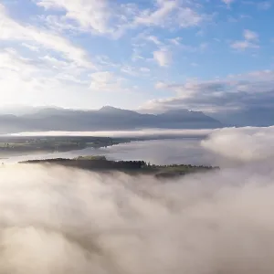 Morning fog hovers over Lake Forggensee with mountains in the background