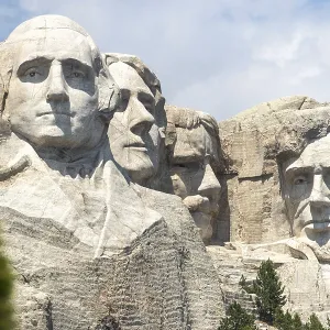 Mount Rushmore with trees in the foreground and a bright sky