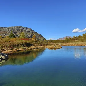 Mountain lake with calm water and surrounding hills under a cloudless sky