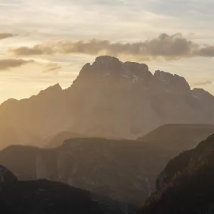 Mountain silhouette during sunset with dramatic clouds and warm light in alpine terrain