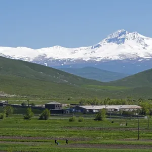A mountain village lies in the middle of green fields in front of a snow-covered mountain range A mountain village lies in the middle of green fields in front of a snow-covered mountain range