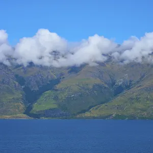 Mountains with a wreath of clouds over a blue lake under a clear sky