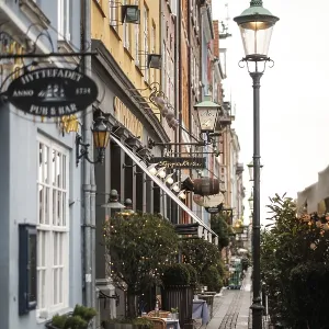 Narrow cobblestone street lined with cafes and colorful buildings under a vintage lamp post in Nyhavn Narrow cobblestone street lined with cafes and colorful buildings under a vintage lamp post in Nyhavn