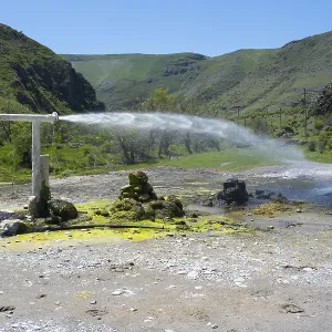 Natural spring with sparkling water jet against green mountain landscape under blue sky Natural spring with sparkling water jet against green mountain landscape under blue sky