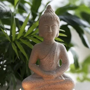 Natural stone statue of Buddha sitting in meditation surrounded by candles and tropical plants