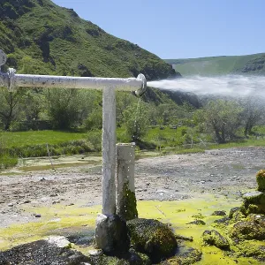 Natural water source with sparkling water jet against green mountain landscape Natural water source with sparkling water jet against green mountain landscape
