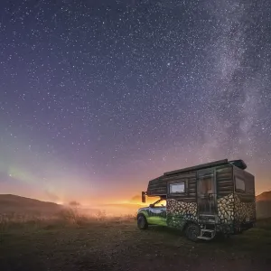 Night shot of a painted camper van under the Milky Way with northern lights