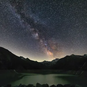 Night sky with Milky Way over mountains and a calm lake in the foreground