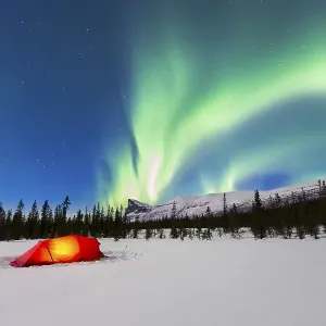 Northern Lights (Aurora borealis) above a red illuminated tent in winter
