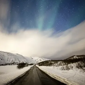 Northern lights over road with snow mountains