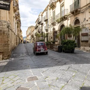 Noto, Sizilien - Italy - 04-06-2025: Red vintage Fiat 500 drives up a narrow stone street in Noto