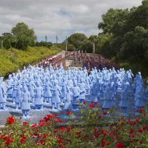Numerous blue terracotta soldier statues stand on a path lined with flowers and trees