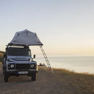 Off-road four-wheel drive vehicle with rooftop tent camping along the Baltic Sea at sunrise in summer Off-road four-wheel drive vehicle with rooftop tent camping along the Baltic Sea at sunrise in summer