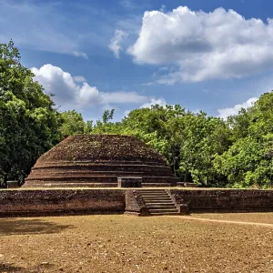 An old brick stupa surrounded by thick greenery and a cloudy sky An old brick stupa surrounded by thick greenery and a cloudy sky