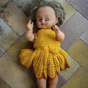 Old doll in orange woolen dress lying on the floor Old doll in orange woolen dress lying on the floor