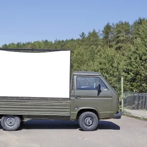 An old no name green army truck with a empty billboard set in a pine forest