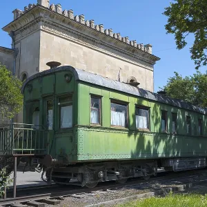 Old green railroad car in front of historic building and trees