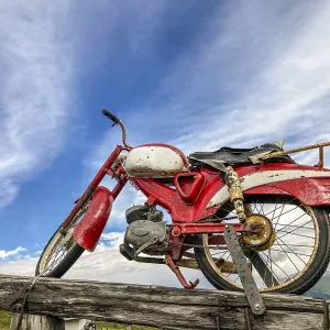 An old rusty red motorcycle stands on a wooden pole