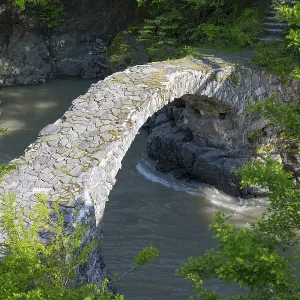 An old stone bridge spans a river amid green trees and rocks