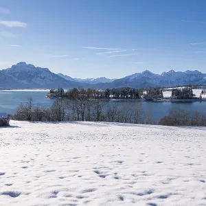 Panorama of a snowy field with lake and mountains under a clear blue sky