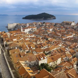 Panorama de la ciudad vieja del Mediterráneo de Dubrovnik con tejas naranjas, pasarela en la muralla fortificada y vista al océano y la isla Lokrum, Croacia.