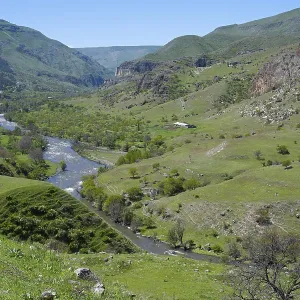 A panoramic view of a green valley with a river surrounded by rolling hills