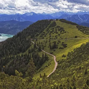 Panoramic view from the Herzogstand of wooded mountains and a winding hiking trail