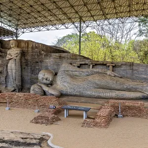 Panoramic view of a large reclining Buddha statue with a figure standing next to it under a protective canopy Panoramic view of a large reclining Buddha statue with a figure standing next to it under a protective canopy