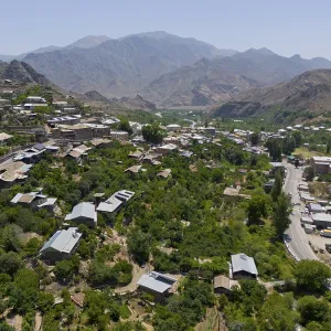 Panoramic view of a village along a road amidst green hills and mountains