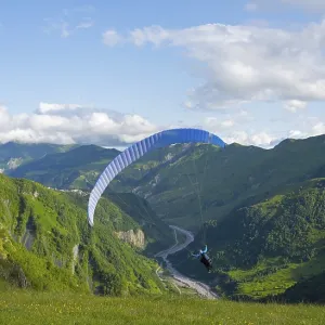 A paraglider soars over a green landscape with wide sky and valley views A paraglider soars over a green landscape with wide sky and valley views