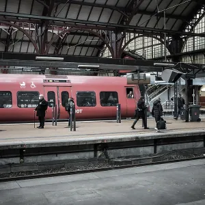 Passengers waiting on a platform beside a red train within a station in Copenhagen Passengers waiting on a platform beside a red train within a station in Copenhagen