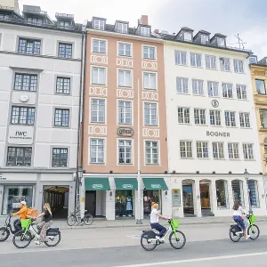 Passers-by ride along on bicycles in front of colourful building facades in Munich