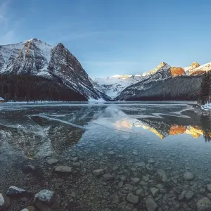 Peaceful lake reflecting snow-capped mountains and a cabin under a clear blue sky at sunrise, Lake Louise, Canadian Rockies Peaceful lake reflecting snow-capped mountains and a cabin under a clear blue sky at sunrise, Lake Louise, Canadian Rockies