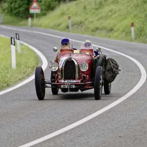 Two people with helmets in a red vintage car on a winding road Two people with helmets in a red vintage car on a winding road