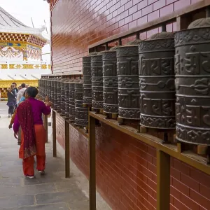 People interact with prayer wheels in a Buddhist-decorated temple with a red and gold accent People interact with prayer wheels in a Buddhist-decorated temple with a red and gold accent