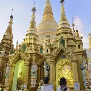 People looking at golden stupas of a temple at sunset