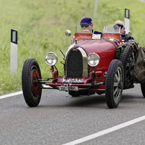 Two people in a red vintage car with racing equipment on a country road Two people in a red vintage car with racing equipment on a country road