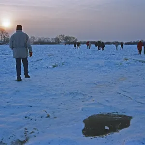 People walk across ice rink, sunset