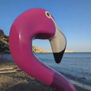 Pink flamingo pedal boat on Tsambika sandy beach with sea in the background at sunset Pink flamingo pedal boat on Tsambika sandy beach with sea in the background at sunset