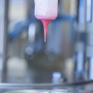 Pink liquid ice cream drips from a machine into a container