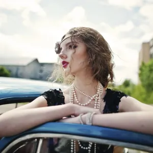 Portrait of beautiful curly fashion girl model with bright makeup in retro style leaned on a vintage car door