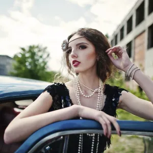 Portrait of beautiful curly fashion girl model with bright makeup in retro style leaned on a vintage car door