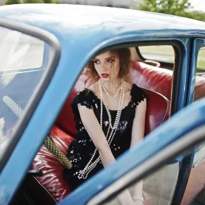 Portrait of beautiful curly fashion girl model with bright makeup in retro style sitting on a vintage car