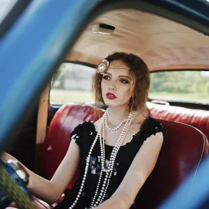 Portrait of beautiful curly fashion girl model with bright makeup in retro style sitting on a vintage car