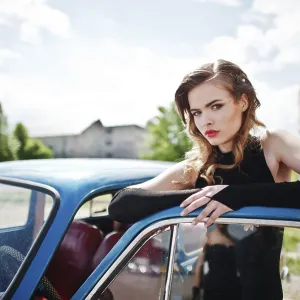 Portrait of beautiful fashion girl model with bright makeup in retro style leaned on a vintage car door