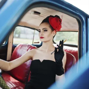 Portrait of beautiful sexy fashion girl model with bright makeup in retro style sitting in vintage car with a cigarette