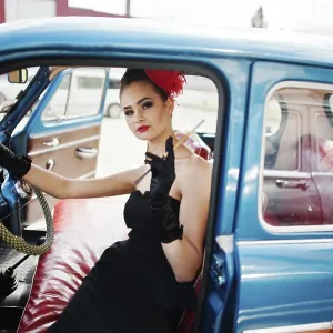 Portrait of beautiful sexy fashion girl model with bright makeup in retro style sitting in vintage car with a cigarette
